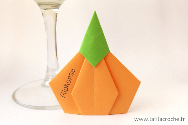 Un marque-place citrouille en origami avec un prénom imprimé sur le côté
