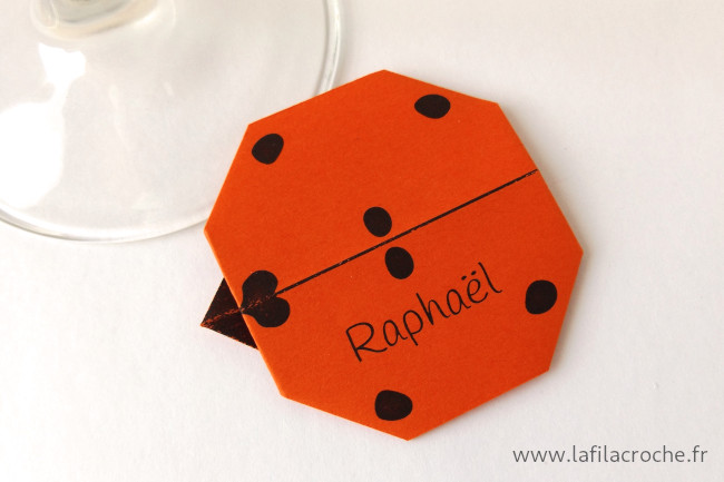 Un marque-place coccinelle rouge orangé en origami personnalisé avec un prénom