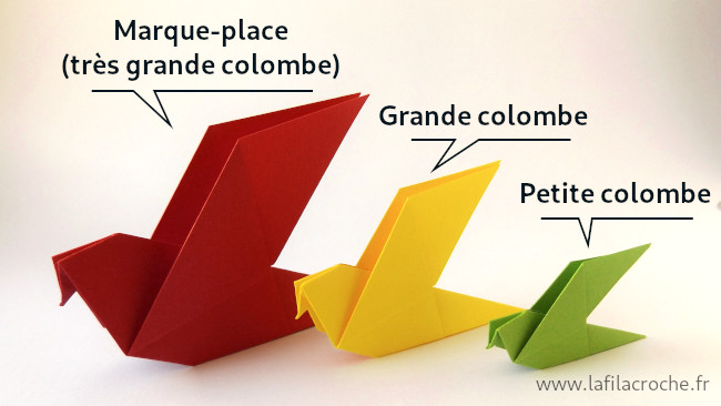 Un marque-place colombe origami posé à côté de deux plus petites colombes