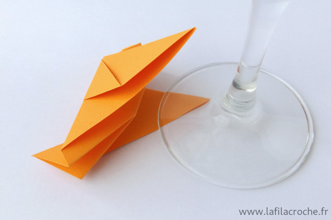 Un marque-place pigeon en origami avec une aile placée sous le pied d’un verre