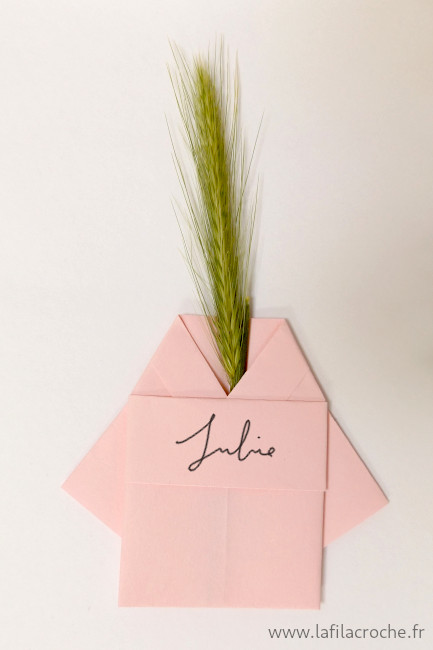 Un marque-place kimono en origami avec un brin d’orge sauvage placé dans le col
