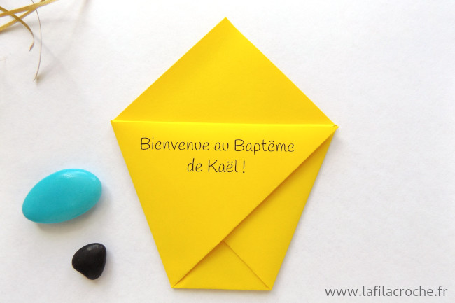 Un marque-place pochette jaune en origami personnalisé avec une phrase de bienvenue pour un baptême