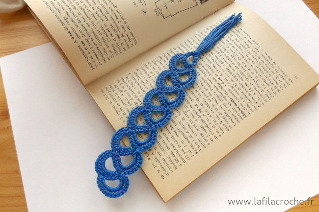 Marque-page arabesque en dentelle bleue au crochet posé sur un livre